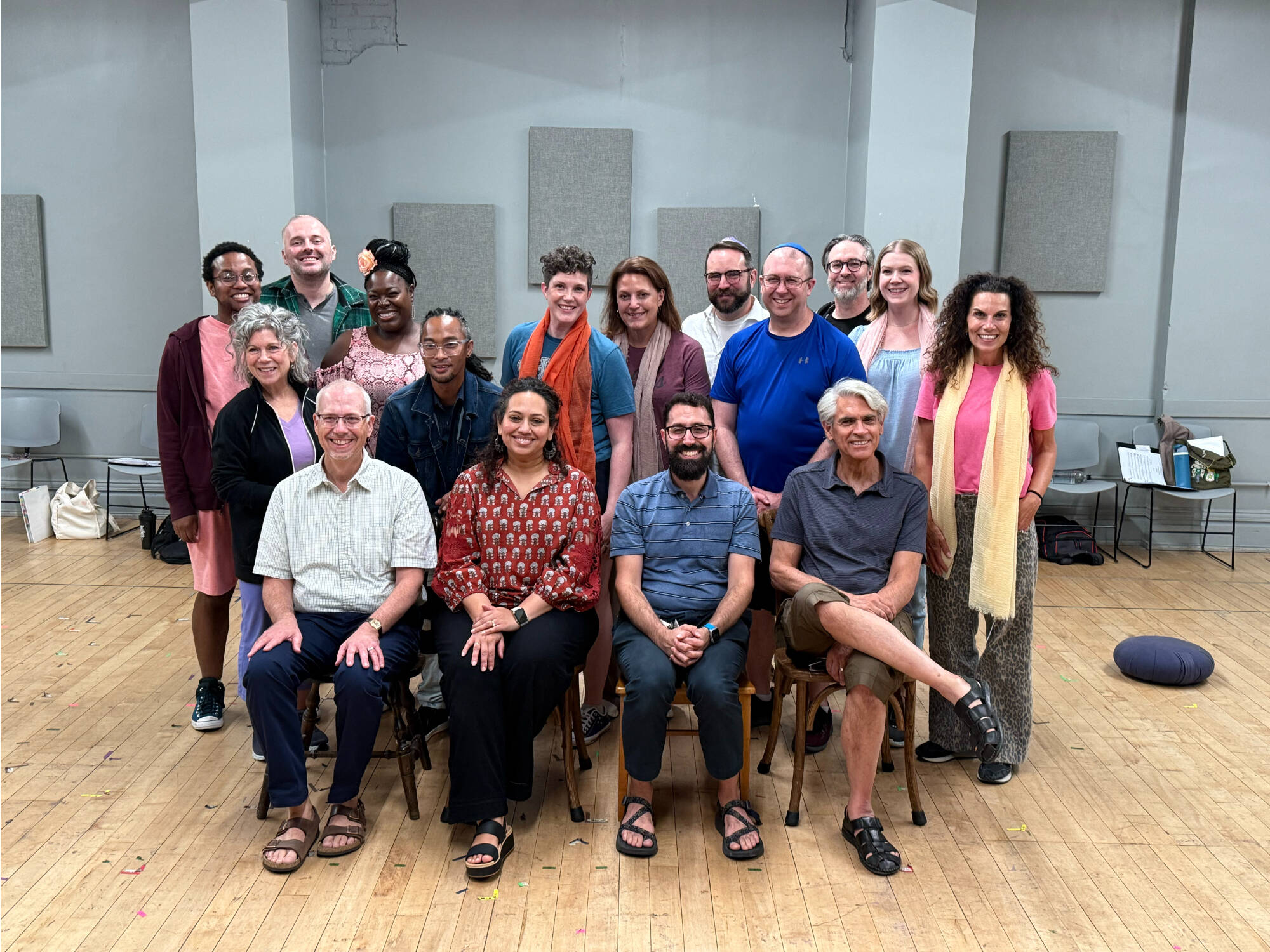 four people seated in chairs with large group of people standing behind them, in Civic Theatre's rehearsal space